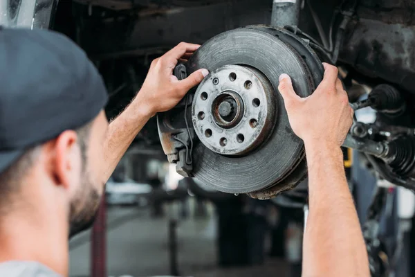 Selective focus of mechanic repairing car without wheel in workshop — Stock Photo