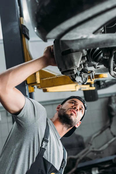 Vista inferior del trabajador en coche de reparación uniforme en taller mecánico - foto de stock