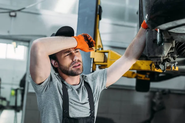 Exhausted mechanic in uniform repairing car in workshop — Stock Photo