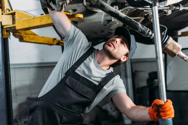 Mécanicien en uniforme travaillant avec la voiture dans l'atelier de réparation automobile — Photo de stock