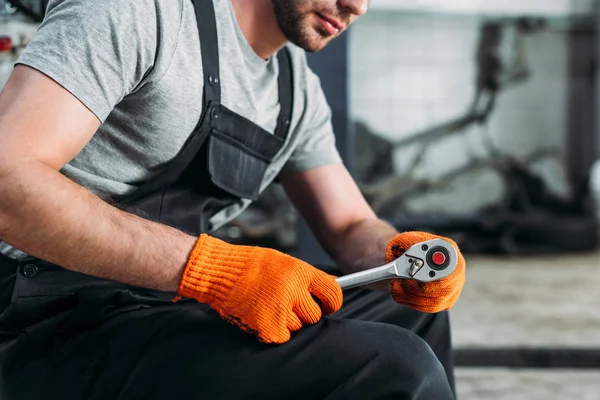 Cropped view of mechanic holding wrench and sitting in auto repair shop — Stock Photo
