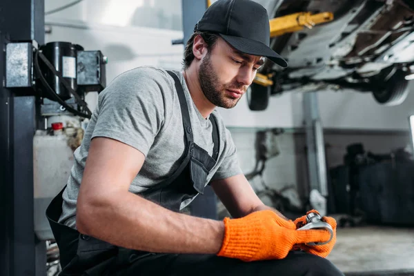 Auto mechanic looking at wrench and sitting in repair shop — Stock Photo