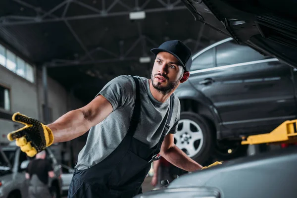 Confused manual worker repairing car in mechanic shop — Stock Photo