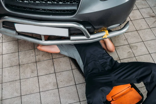 Visão de alto ângulo do trabalhador deitado e trabalhando sob o carro na loja mecânica — Fotografia de Stock