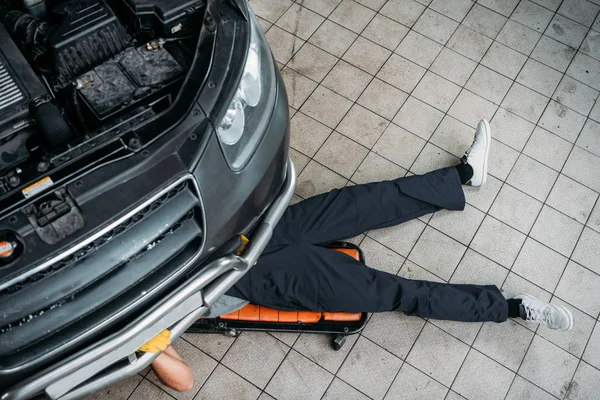 Vue de dessus du mécanicien couché et travaillant sous la voiture — Photo de stock