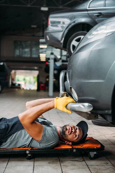 Obrero acostado y trabajando bajo el coche en taller mecánico - foto de stock