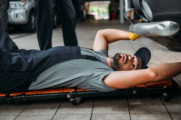 Worker lying and working under car in mechanic shop — Stock Photo