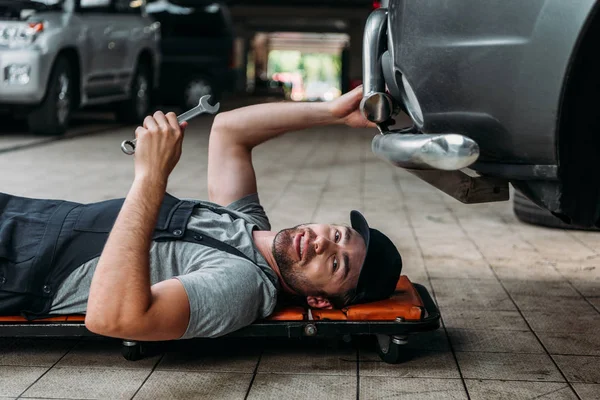 Mechanic lying and working under car in auto repair shop — Stock Photo