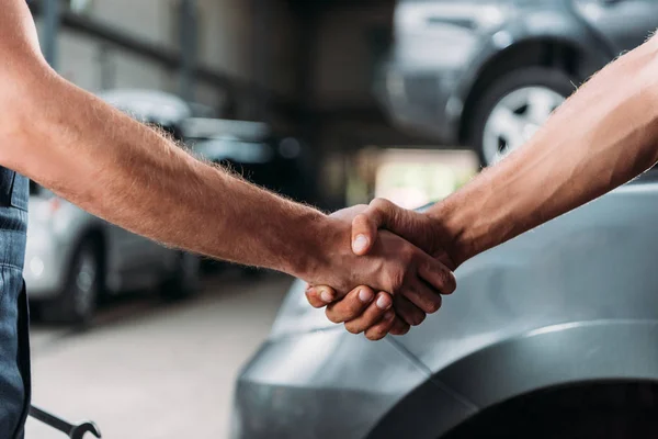 Cropped view of mechanics shaking hands in auto repair shop — Stock Photo