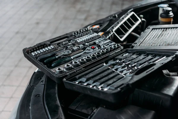 Werkzeugkoffer mit Schraubenschlüsseln und Metallmuttern liegt auf geöffneter Motorhaube in Werkstatt — Stockfoto