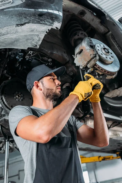 Professional workman fixing car without wheel in mechanic shop — Stock Photo