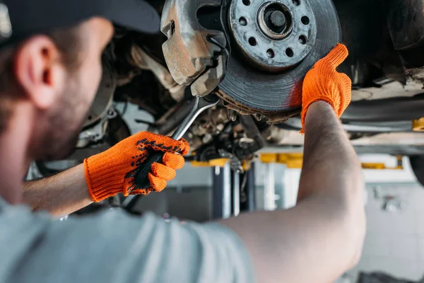 Selective focus of professional worker repairing car without wheel in mechanic shop — Stock Photo
