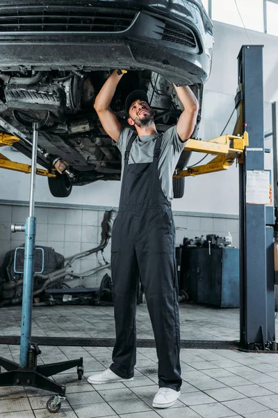 Trabajador profesional en uniforme reparando un coche en taller mecánico - foto de stock