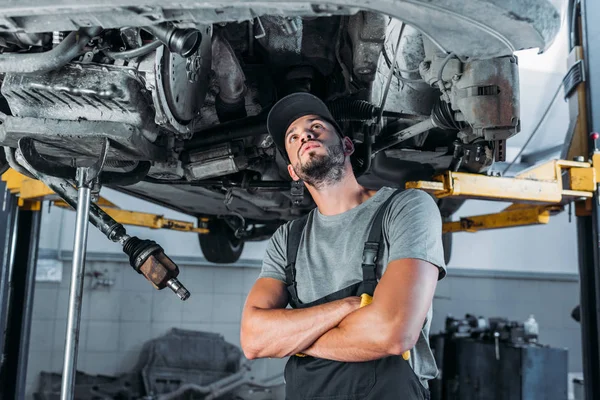 Berufskraftfahrer mit verschränkten Armen schaut Auto in Mechaniker-Werkstatt an — Stockfoto