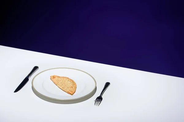 Vista de cerca de pastelería de carne poco saludable en el plato y cubiertos en la mesa sobre fondo azul - foto de stock