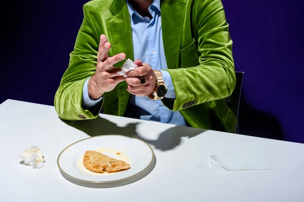 Foto ritagliata dell'uomo in giacca di velluto mani asciugatura con tovagliolo mentre seduto a tavola con cheburek carne sul piatto con sfondo blu — Foto stock