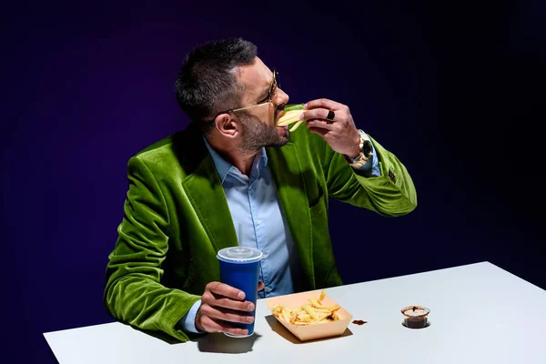 Élégant homme en velours veste avec soda boisson manger frites avec ketchup à table avec fond bleu — Photo de stock