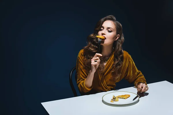 Schöne Frau in stilvoller Kleidung isst Fleischgebäck am Tisch mit blauem Hintergrund — Stockfoto