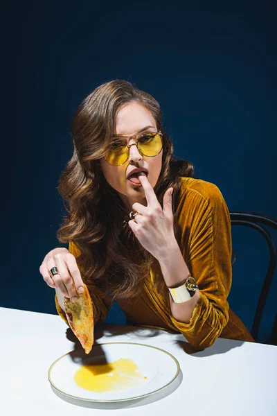 Portrait de femme à la mode avec une pâtisserie de viande malsaine assise à table avec fond bleu — Photo de stock