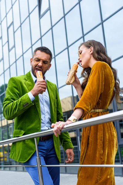 Couple in luxury outfit eating french hot dogs on street — Stock Photo