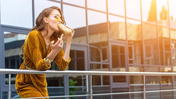 Femme en robe à la mode manger hot dog français et montrant majeur doigt sur la rue — Photo de stock