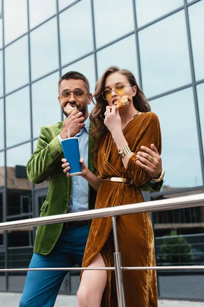 Porträt eines modischen Paares in Samtkleidung, das auf der Straße gebratene Hühnerkeulen isst — Stockfoto