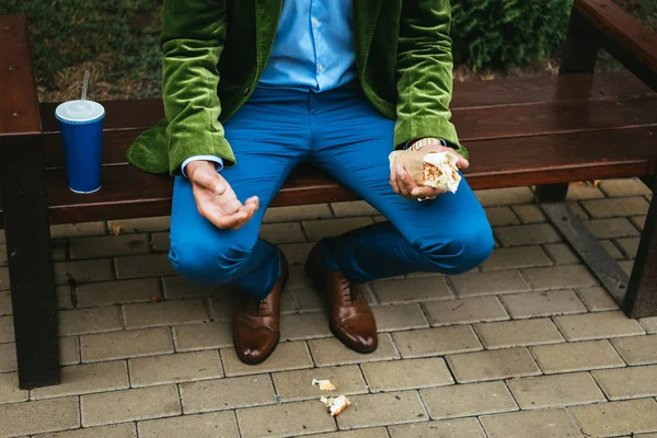 Частковий вид людини в модному одязі з шаурмою, що сидить на лавці на вулиці — стокове фото