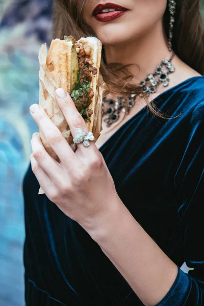 Partial view of woman in stylish clothing holding hot dog in hand on street — Stock Photo