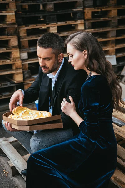 Vista laterale di coppia elegante con pizza al formaggio italiano appoggiata sulla strada — Foto stock