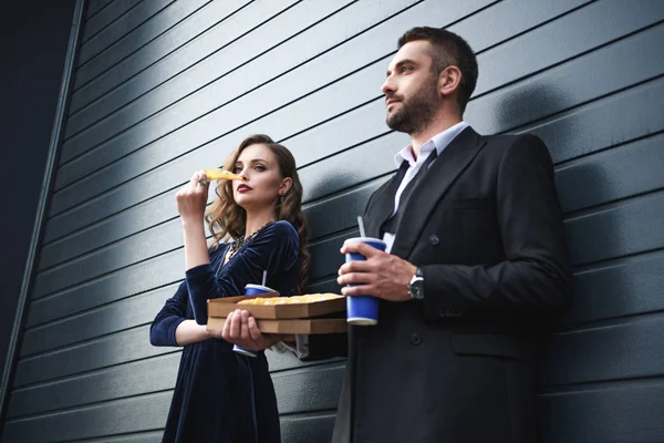 Vue latérale du couple en tenue de luxe avec boissons gazeuses et pizza italienne dans la rue — Photo de stock