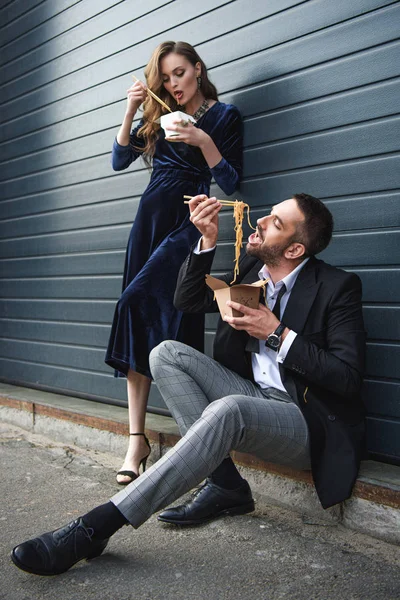 Couple in fashionable clothing eating asian takeaway food on street — Stock Photo