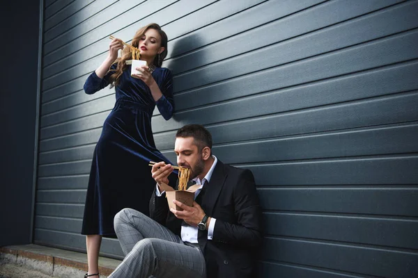 Пара в модной одежде ест азиатскую еду на вынос на улице — стоковое фото