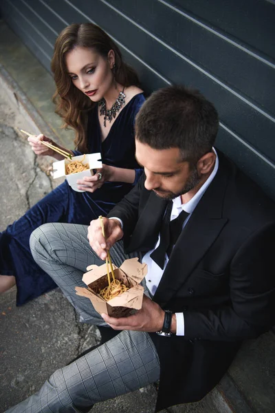 Ángulo alto vista de pareja en ropa de moda con comida para llevar asiática en la calle - foto de stock