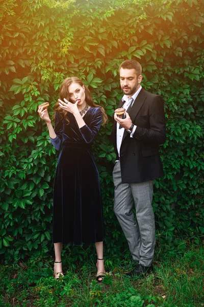 Pareja de moda con donas de chocolate con follaje verde detrás - foto de stock