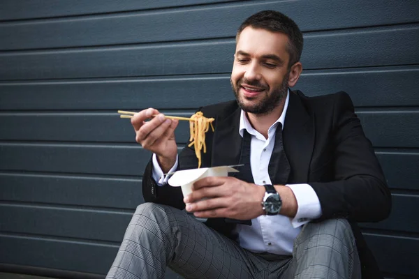 Retrato de hombre sonriente en traje elegante con palillos y comida asiática en la calle - foto de stock