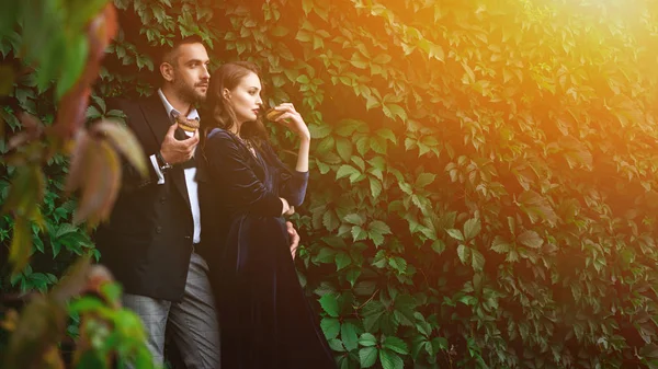 Fashionable couple with chocolate doughnuts with green foliage behind — Stock Photo