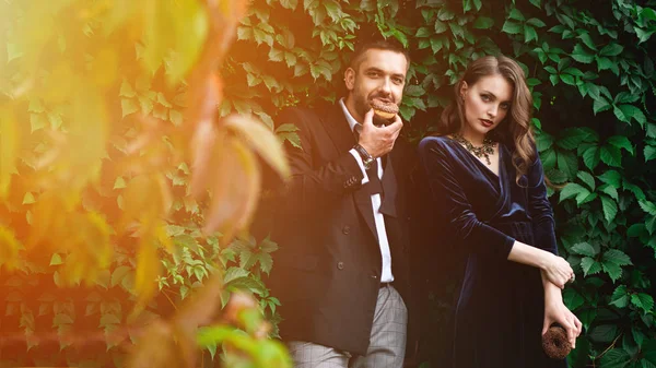 Retrato de pareja de moda con rosquillas de chocolate con follaje verde detrás - foto de stock