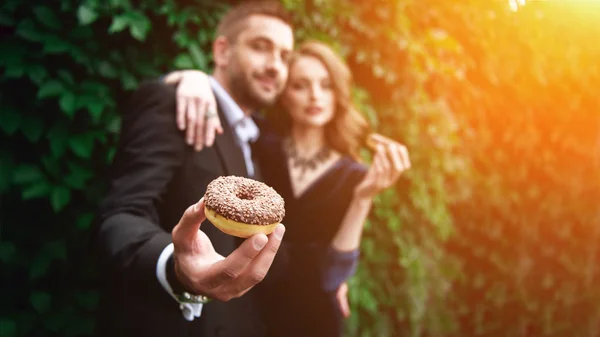 Selective focus of fashionable couple with chocolate doughnuts with green foliage behind — Stock Photo