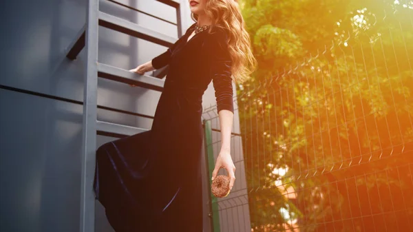 Cropped shot of woman in luxury dress with chocolate doughnut in hand hanging on ladder on street — Stock Photo