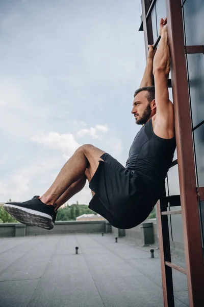 Vista lateral del deportista guapo haciendo ejercicio en la escalera en el techo - foto de stock