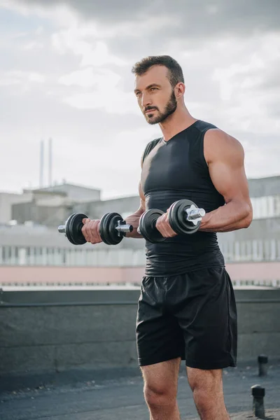 Handsome sportsman training with dumbbells on roof — Stock Photo