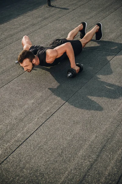 Apuesto deportista haciendo flexiones con mancuernas en el techo - foto de stock