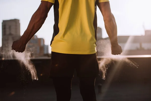 Image recadrée du sportif avec de la poudre de talc dans les mains debout sur le toit — Photo de stock