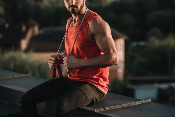 Обрізане зображення спортсмена зі стрибковою мотузкою на шиї, що сидить на даху — стокове фото