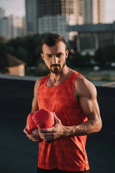 Красивий спортсмен тримає рукавички червоного боксу на даху — стокове фото