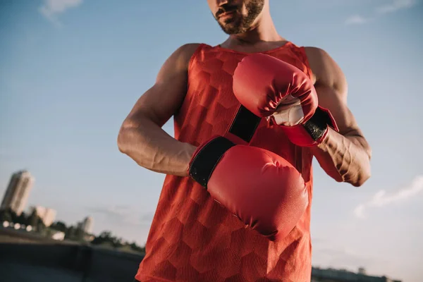 Abgeschnittenes Bild eines Sportlers, der rote Boxhandschuhe auf dem Dach bindet — Stockfoto