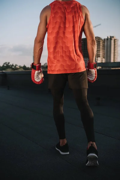 Vue arrière du sportif marchant avec des gants de boxe sur le toit — Photo de stock