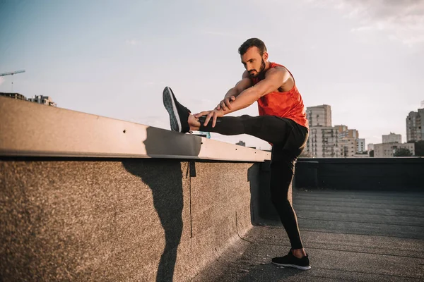 Apuesto deportista estirar piernas en el techo - foto de stock