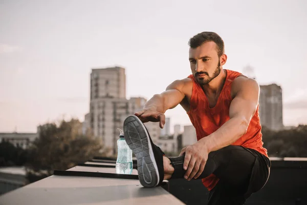 Handsome athletic sportsman stretching legs on roof — Stock Photo