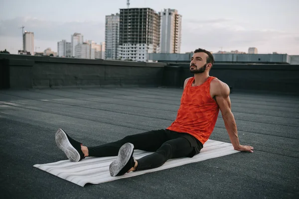 Schöner Sportler ruht sich nach dem Training auf dem Dach auf der Yogamatte aus — Stockfoto